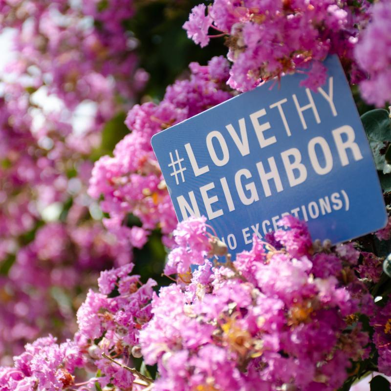 Love thy Neighbor sign in flowering tree